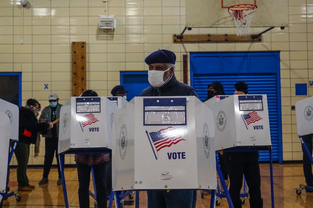 A Black voter behind a privacy screen, wearing a mask